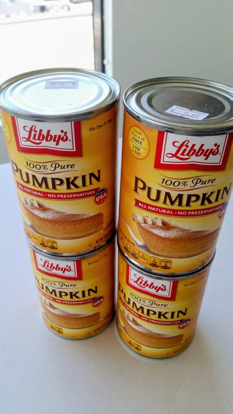 Four cans of pumpkin purée stacked two by two on a counter, with price stickers on their lids